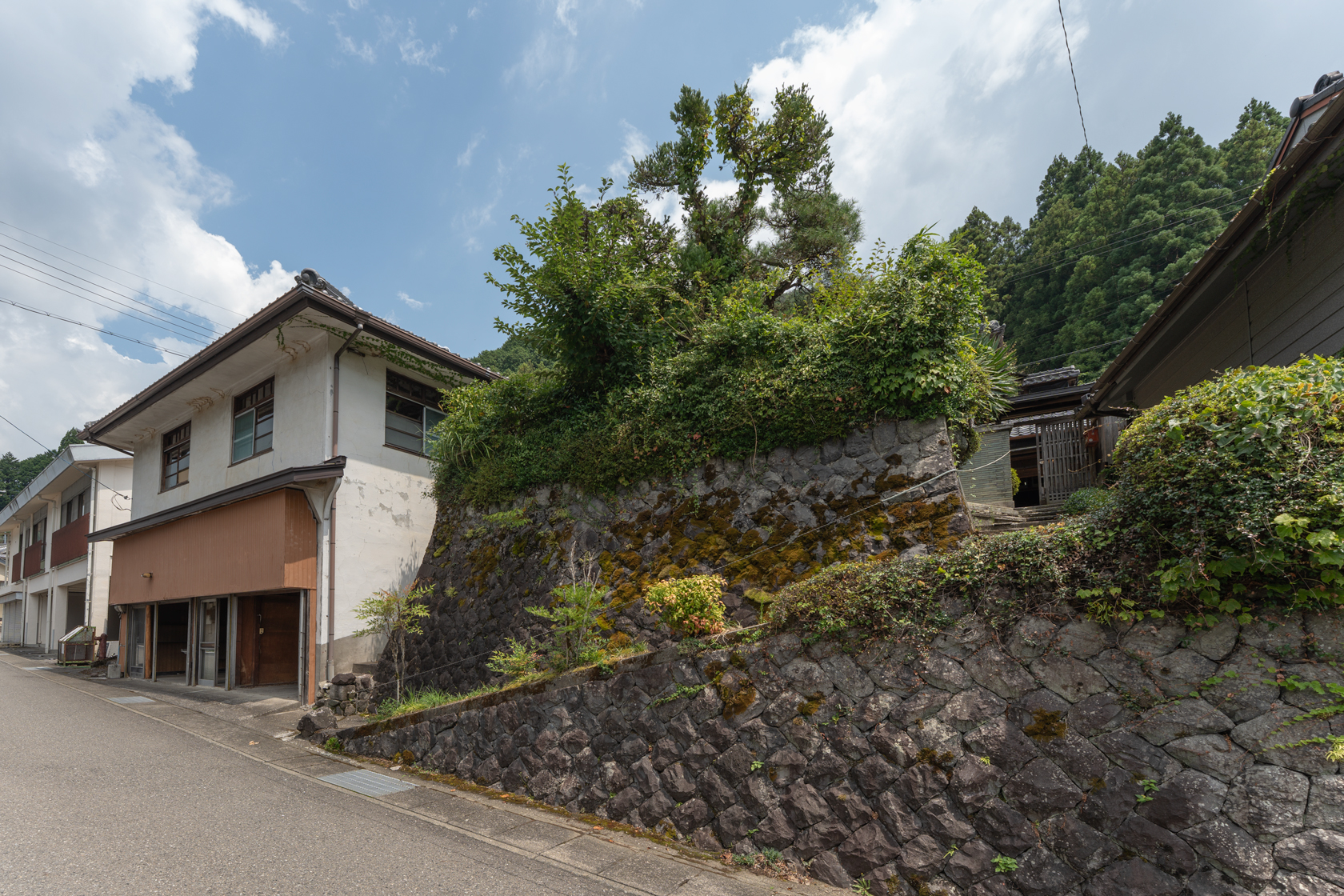 奈良県十津川村大字上野地：外観全景。石垣の擁壁の上に建つ建物と道路。